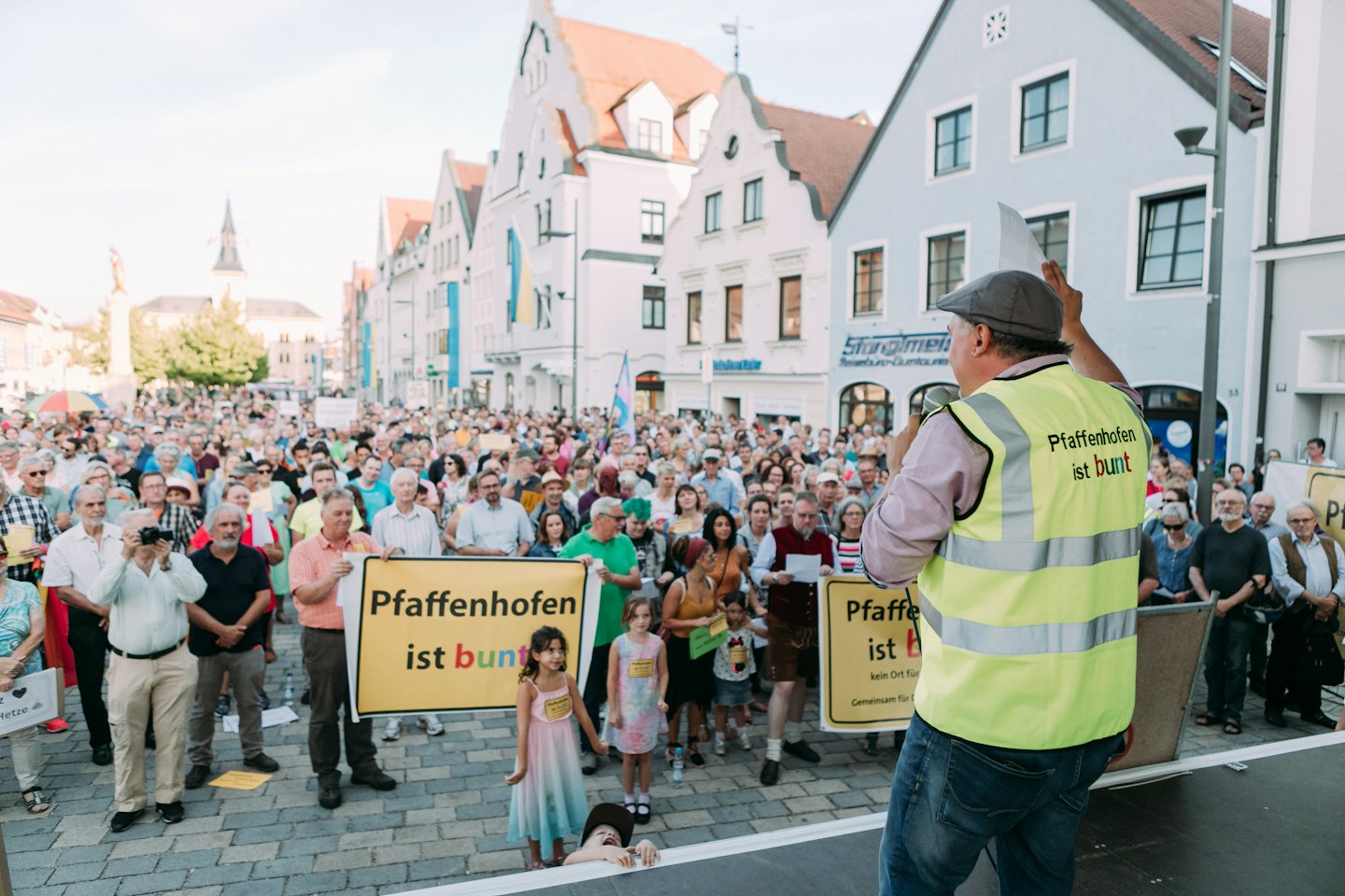 Ein Redner in einer gelben Weste spricht zu einer Menge, die Banner hält.