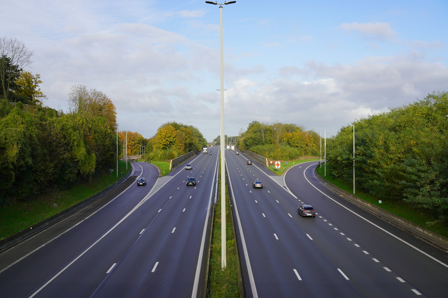 Mehrspurige Autobahn mit Zubringerstraßen in einer von Bäumen gesäumten Landschaft.