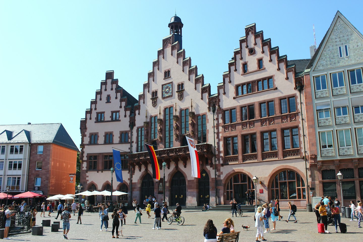 Menschen gehen über einen historischen europäischen Stadtplatz mit Giebelhäusern.