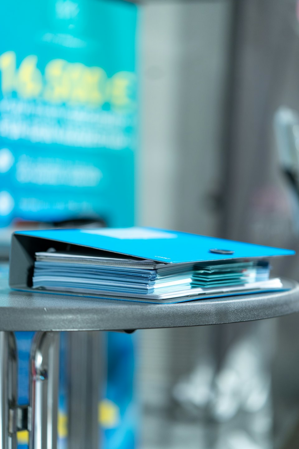 Blaue Broschüren liegen in einem schwarzen Ordner auf einem Tisch.